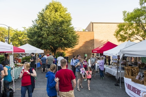 A crowd mingles outdoors between vendor tents at the Ravenswood Farmers Market