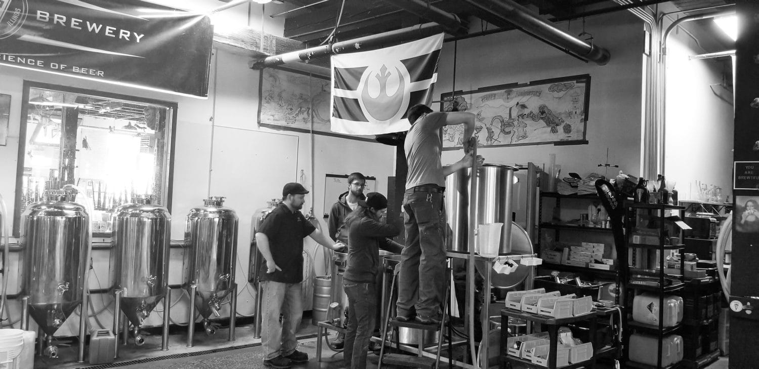 A picture of a group of brewers huddled over brewing equipment