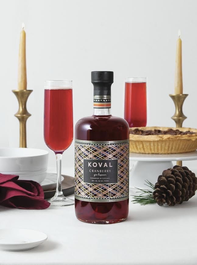 A photo of a bottle of KOVAL Cranberry Gin and some champagne flutes filled with cranberry gin spritzers