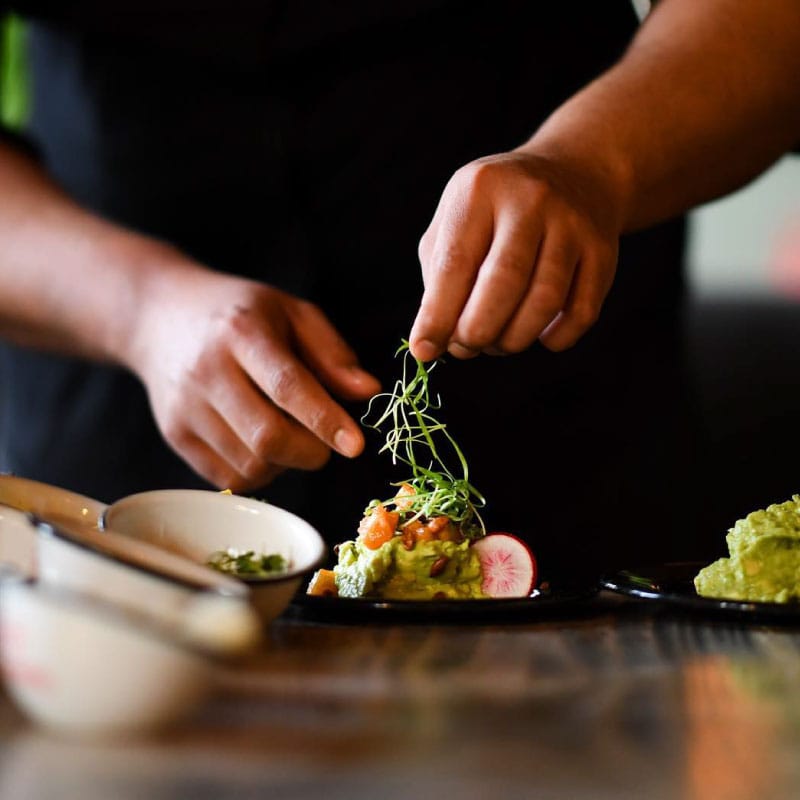 A photo of a chef carefully plating a dish of spicy pumpkin seed guacamole
