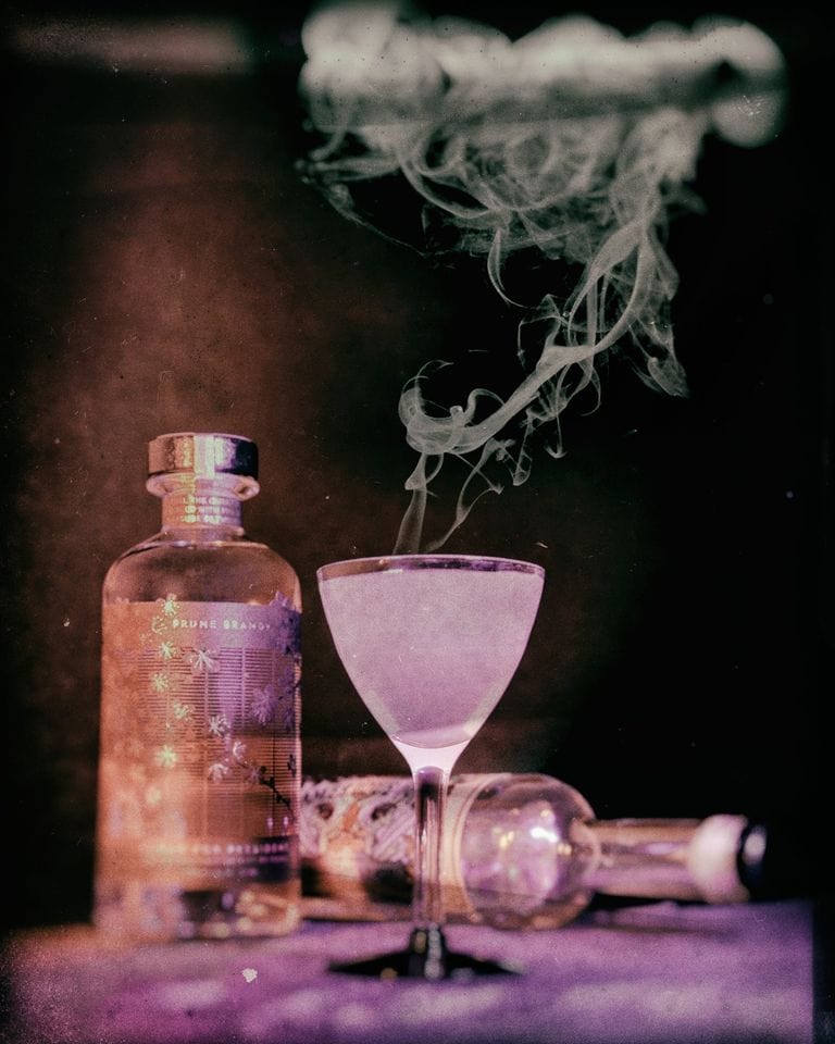 A cloudy KOVAL Halloween cocktail billowing smoke in front of a bottle of KOVAL gin