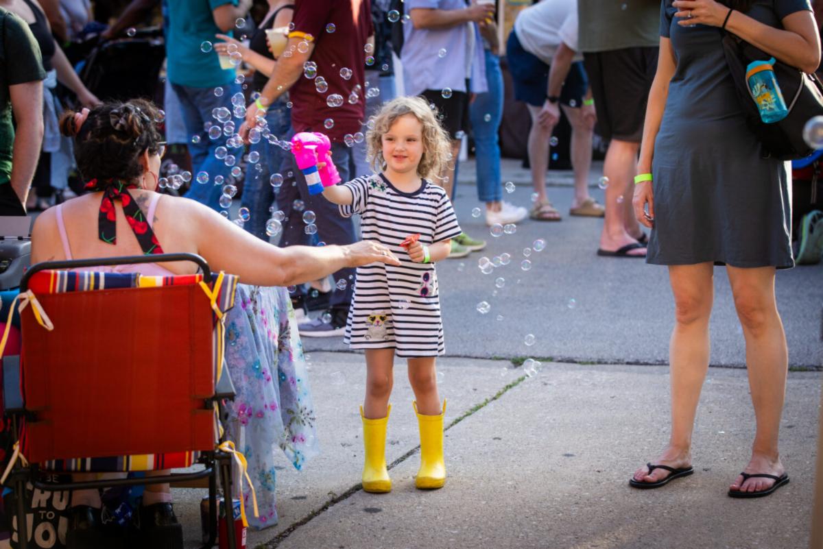 A young girl blows bubbles in yellow boots